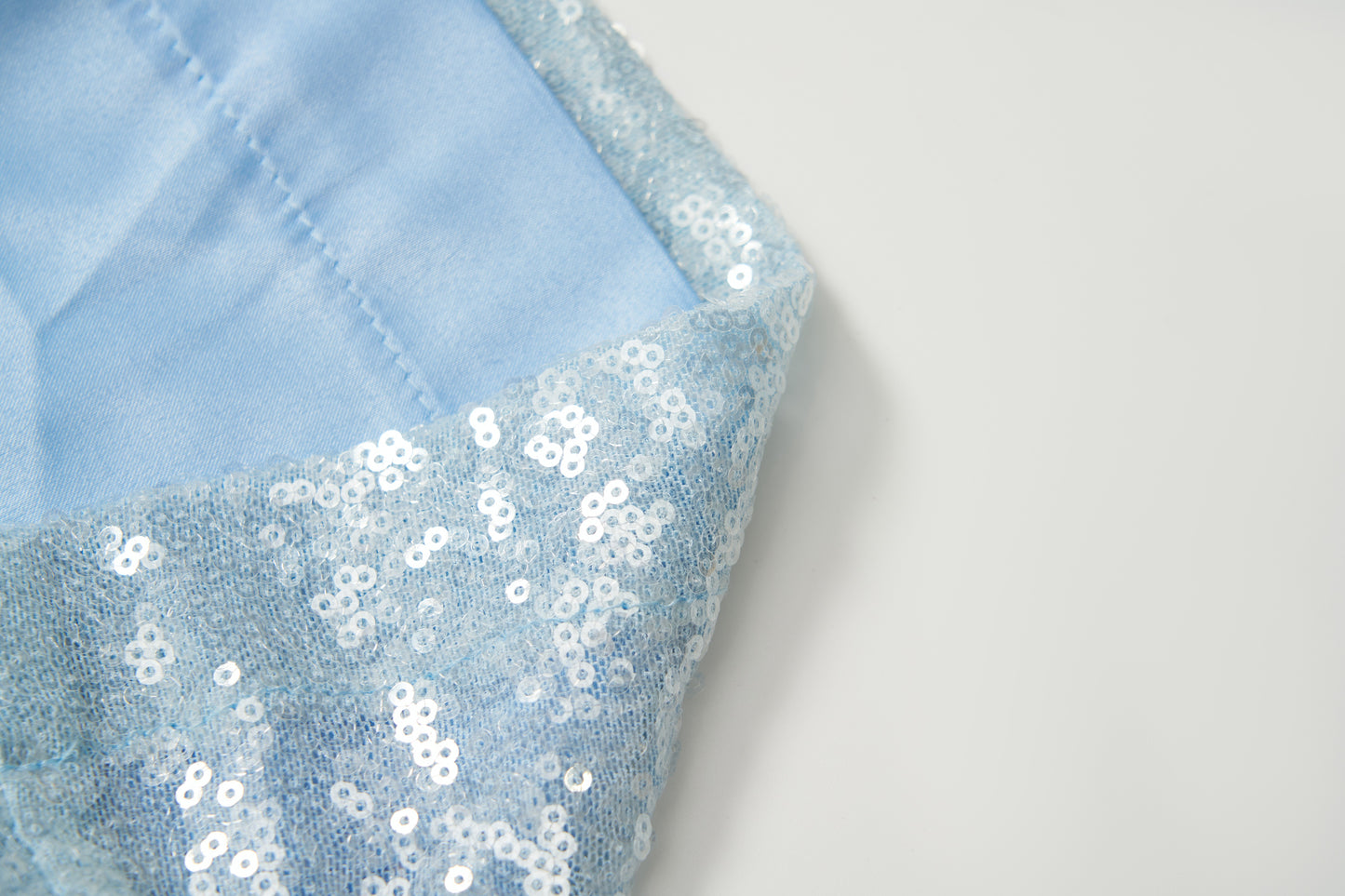 Close-up of light blue fabric embellished with shiny white sequins, reflecting the elegant detail of KIKI and JOJO's Radiance Sequin Wide-leg Pants, set against a plain white background.