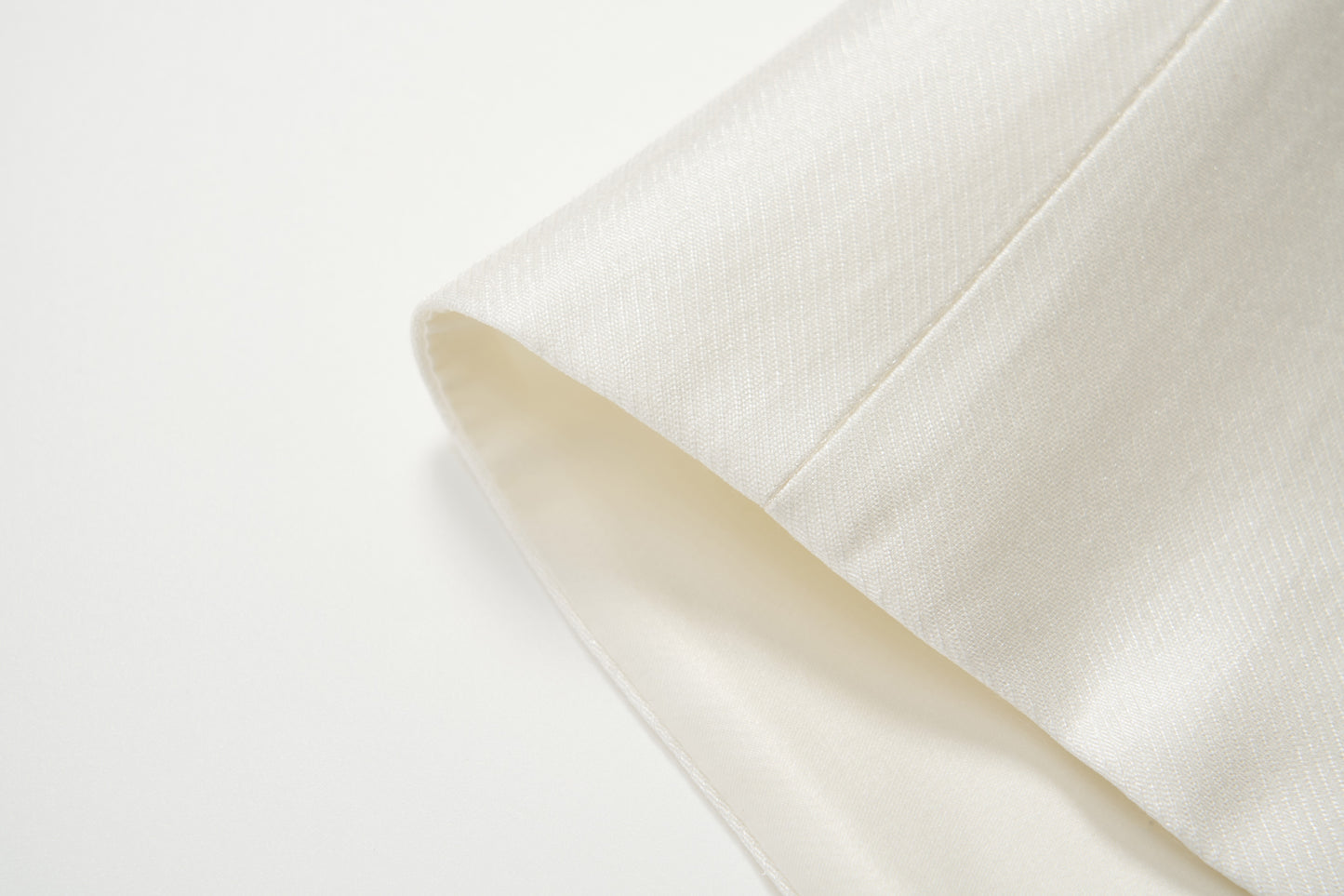 Close-up of the cuff of the cream-colored Radiance Satin Crop Top by KIKI and JOJO, featuring smooth, textured satin fabric and long sleeves, shown against a white background.