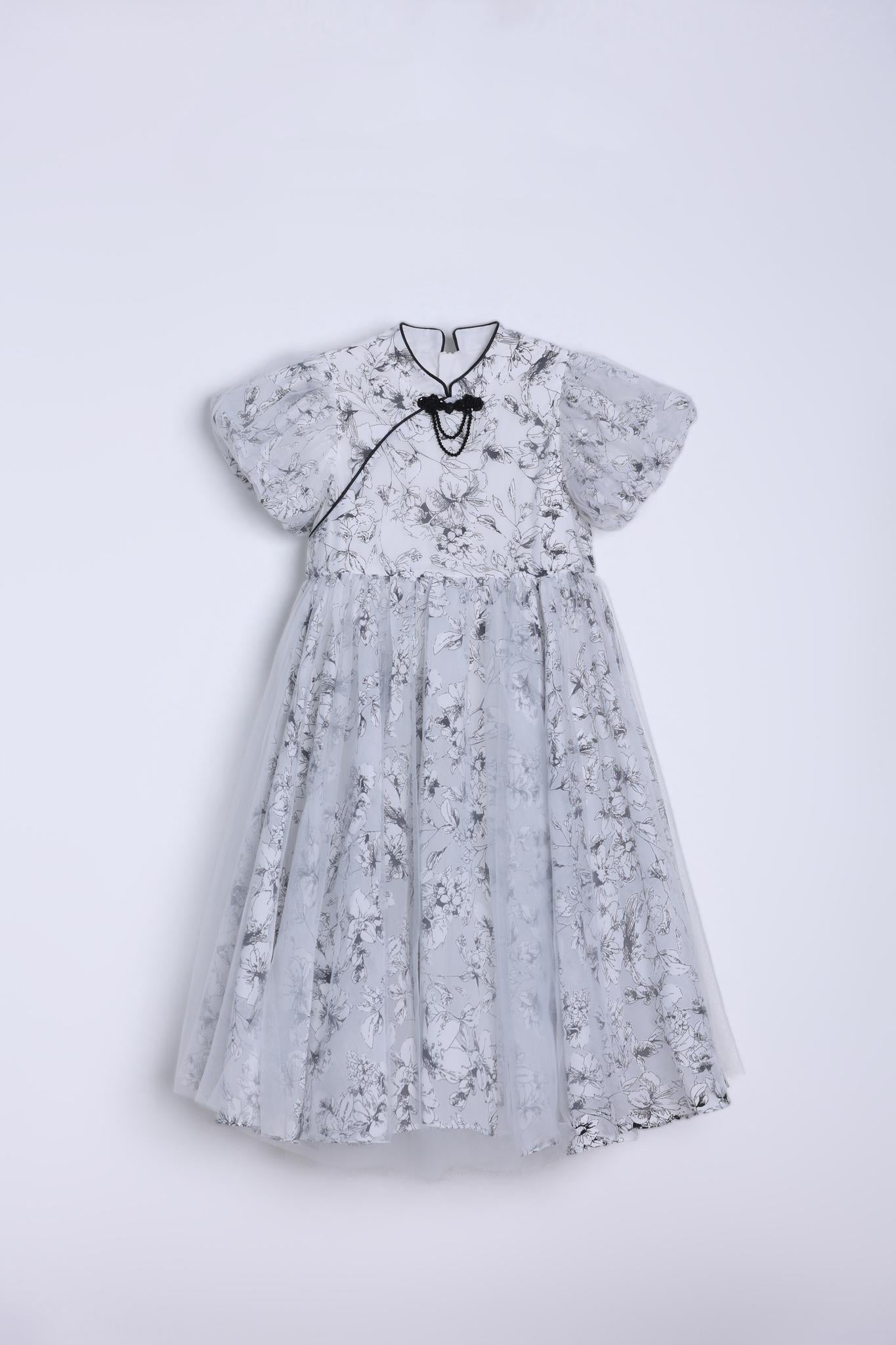 The KIKI and JOJO Girls Cheongsam Dress – Ethereal Blossom Puff Sleeve Tulle is a floor-length white dress with a delicate floral pattern and full tulle skirt, shown on a hanger against a plain white background.