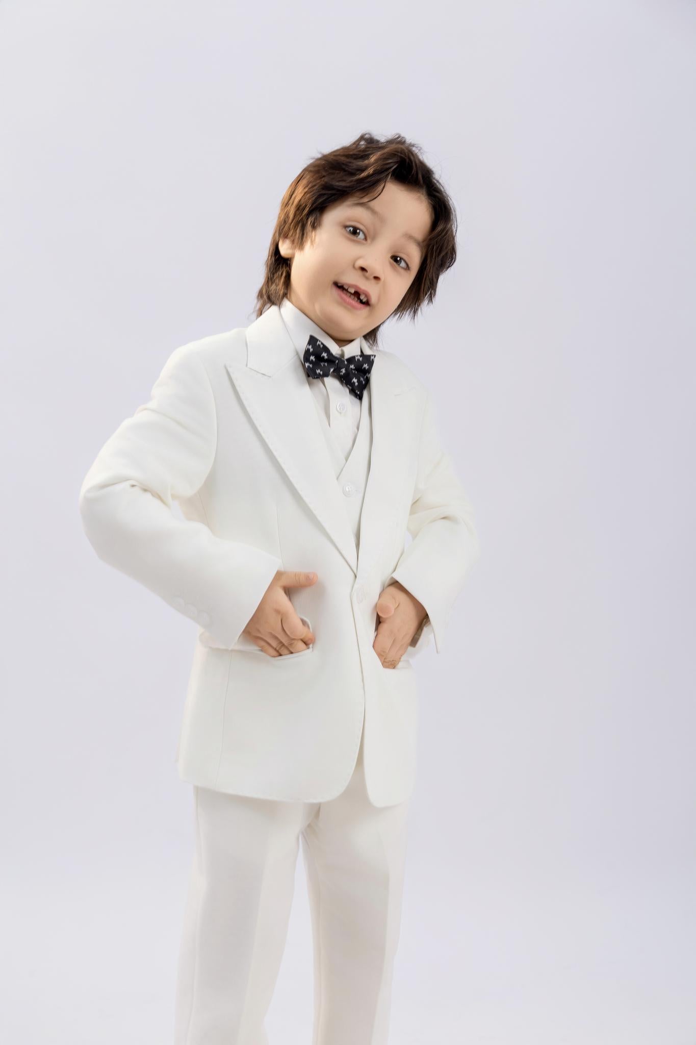 A young boy models the KIKI and JOJO Kids Suit Vest – White (3-14 Years), a classic fit, wrinkle-free vest, paired with a black polka dot bow tie. He stands confidently against a plain light background, hands on hips, looking at the camera.