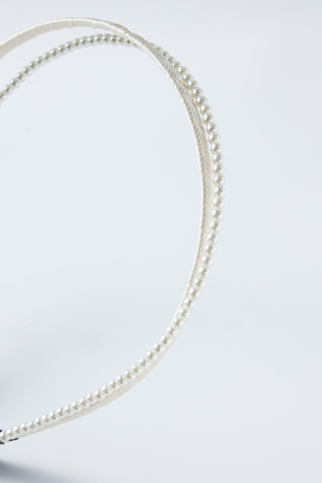 The KIKI and JOJO Girls Dainty Pearl Headband – Pure White, adorned with a row of small faux pearls, is displayed against a plain light background.