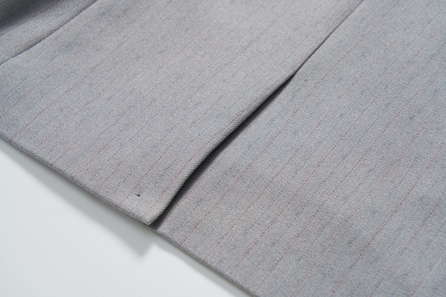 Close-up of the Silver Bloom Suit Jacket by KIKI and JOJO, showing its light gray pinstripe fabric with a seam and pleat, displayed on a white surface.