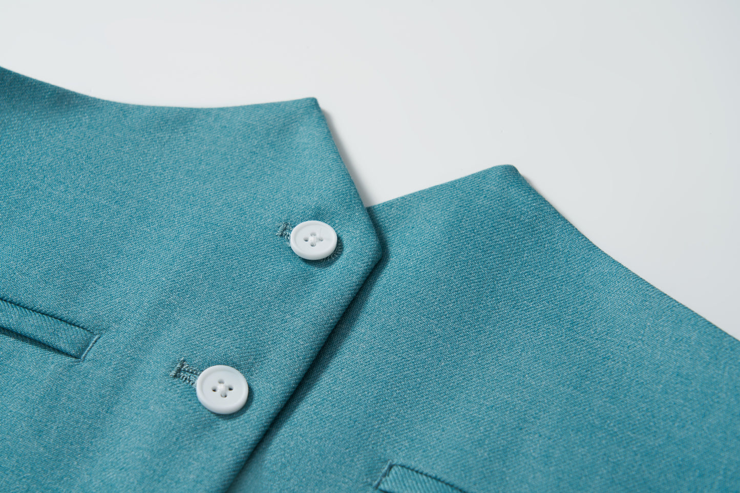 Close-up of the Celeste Whimsy Suit Vest by KIKI and JOJO—a peacock blue boys' vest with two white buttons and a pocket—displayed on a white background.