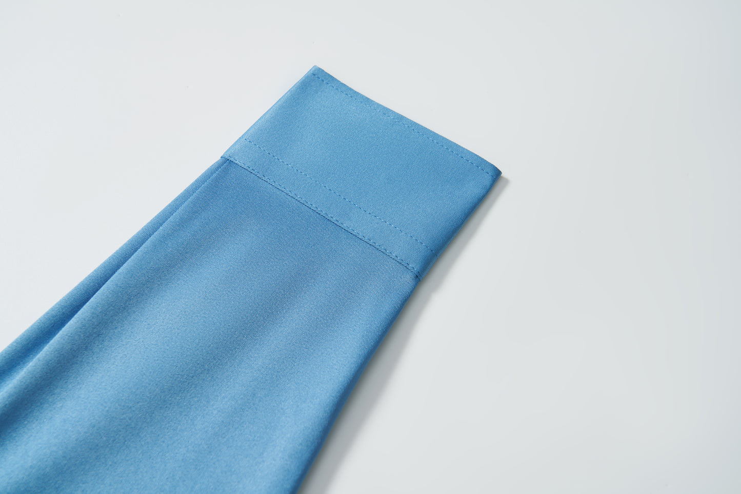 A close-up of the KIKI and JOJO Boys Sky Blue Dress Shirt, neatly folded with visible stitching, displayed on a white background.