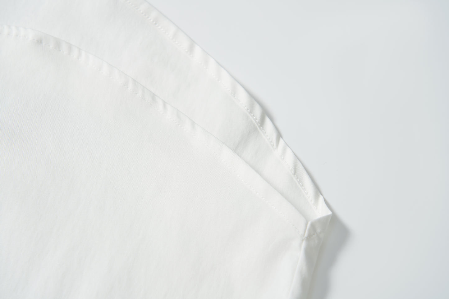 Close-up of the corner and stitched hem of the Moonlit Whisper Blouse by KIKI and JOJO, showcasing delicate, scalloped details against a plain white background.