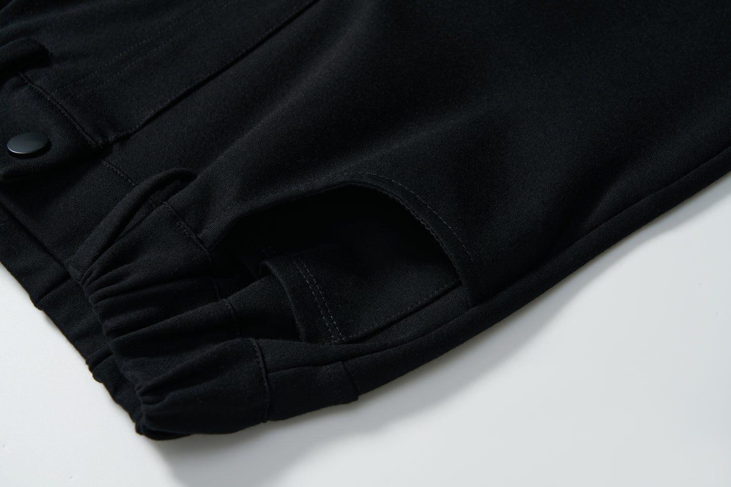 Close-up of the Petal Whisper Dress Pants by KIKI and JOJO, featuring a flared black design, elastic waistband, snap button, and side pocket. Crafted from stretchy fabric and displayed flat on a white background.
