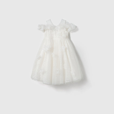 The Feathered Whisper Dress by KIKI and JOJO is a white sleeveless off-shoulder A-line dress for girls, featuring a tulle overlay, floral appliqués, and ruffle details, shown on a plain light background.