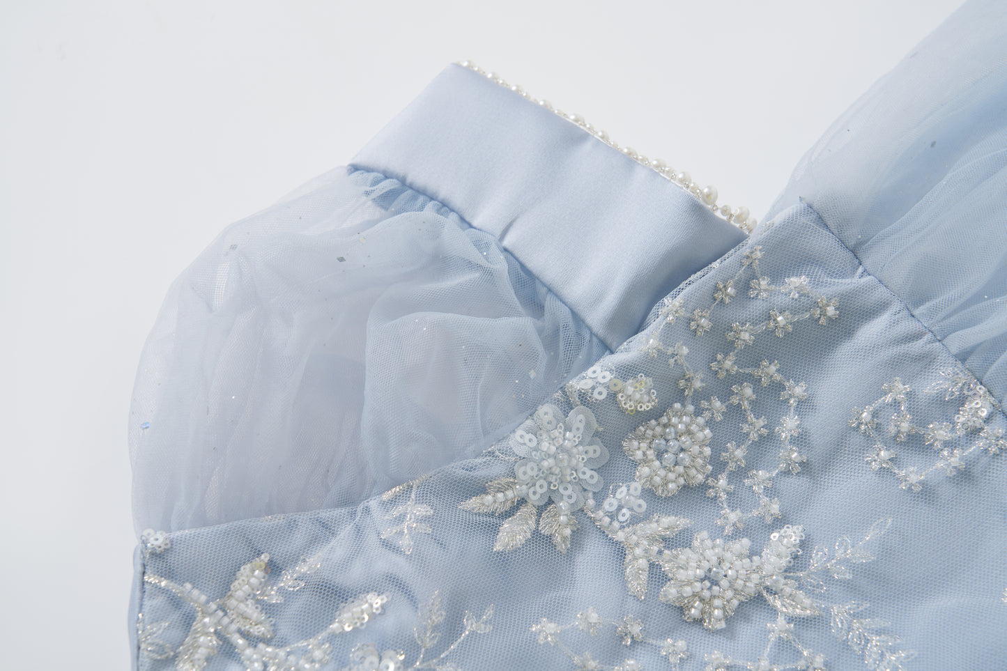 Close-up of the Mist Whisper Dress by KIKI and JOJO in pale blue, featuring pearl trim, sheer puff sleeves, and delicate hand-embroidered floral details with sequins and beads.