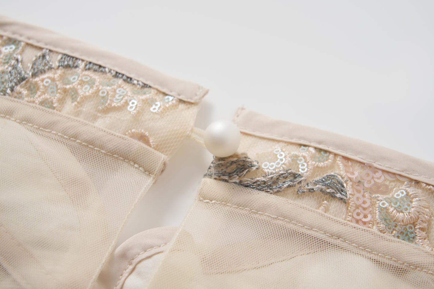 Close-up of the Jade Whisper Dress by KIKI and JOJO, featuring two sheer fabric panels with embroidered florals and metallic accents, joined by a pearl button—capturing the delicate elegance inspired by the cheongsam.