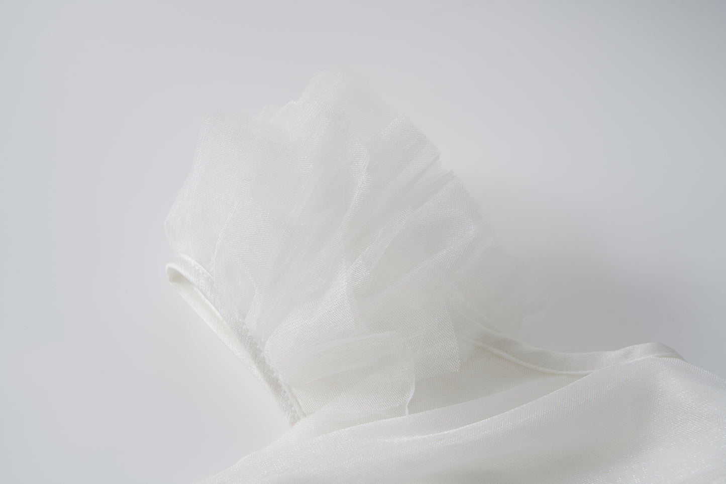 Close-up of the Cloud Whisper Dress by KIKI and JOJO, showcasing sheer white tulle layers arranged in ruffles against a smooth, light background.