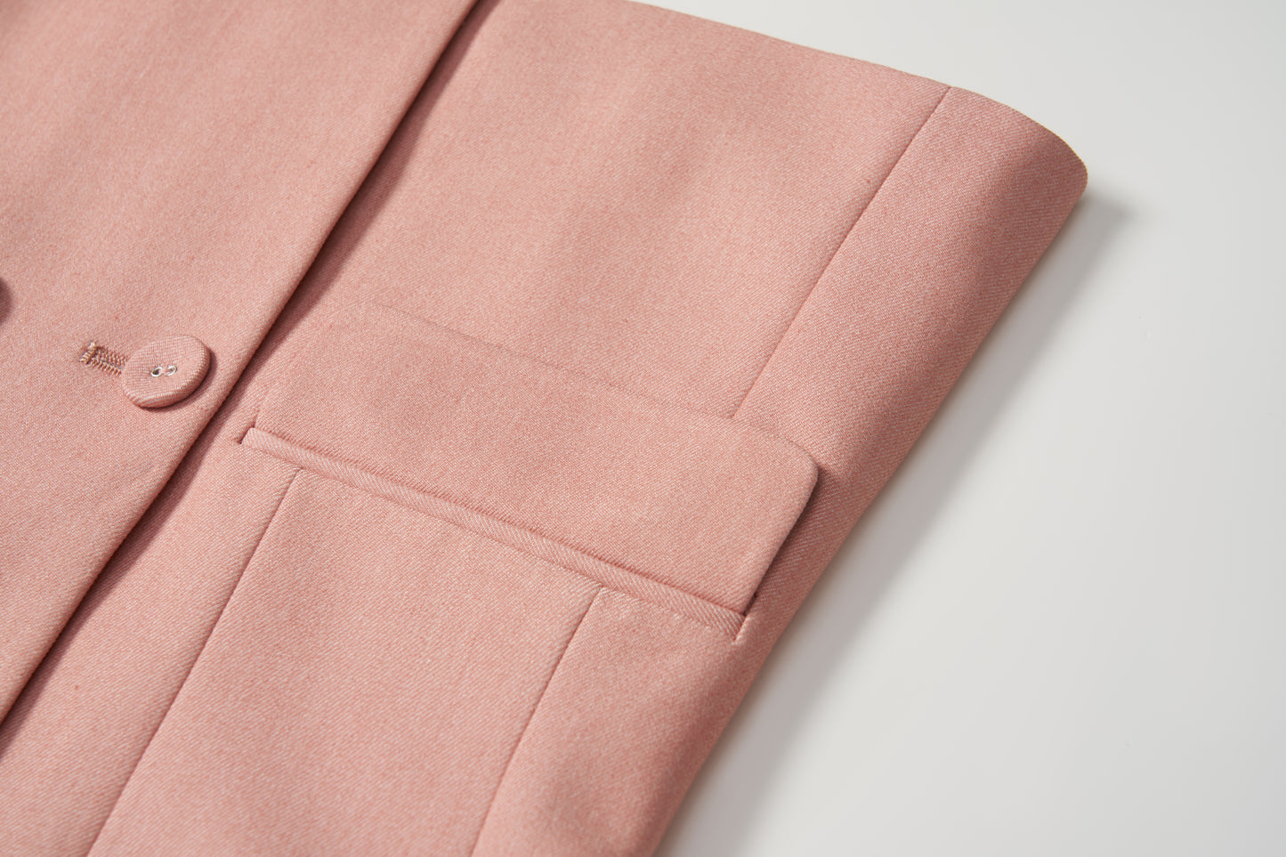Close-up of the Blush Reverie Suit Jacket by KIKI and JOJO, showing the blush pink sleeve and pocket on a white surface, with focus on the button detail and fabric texture.
