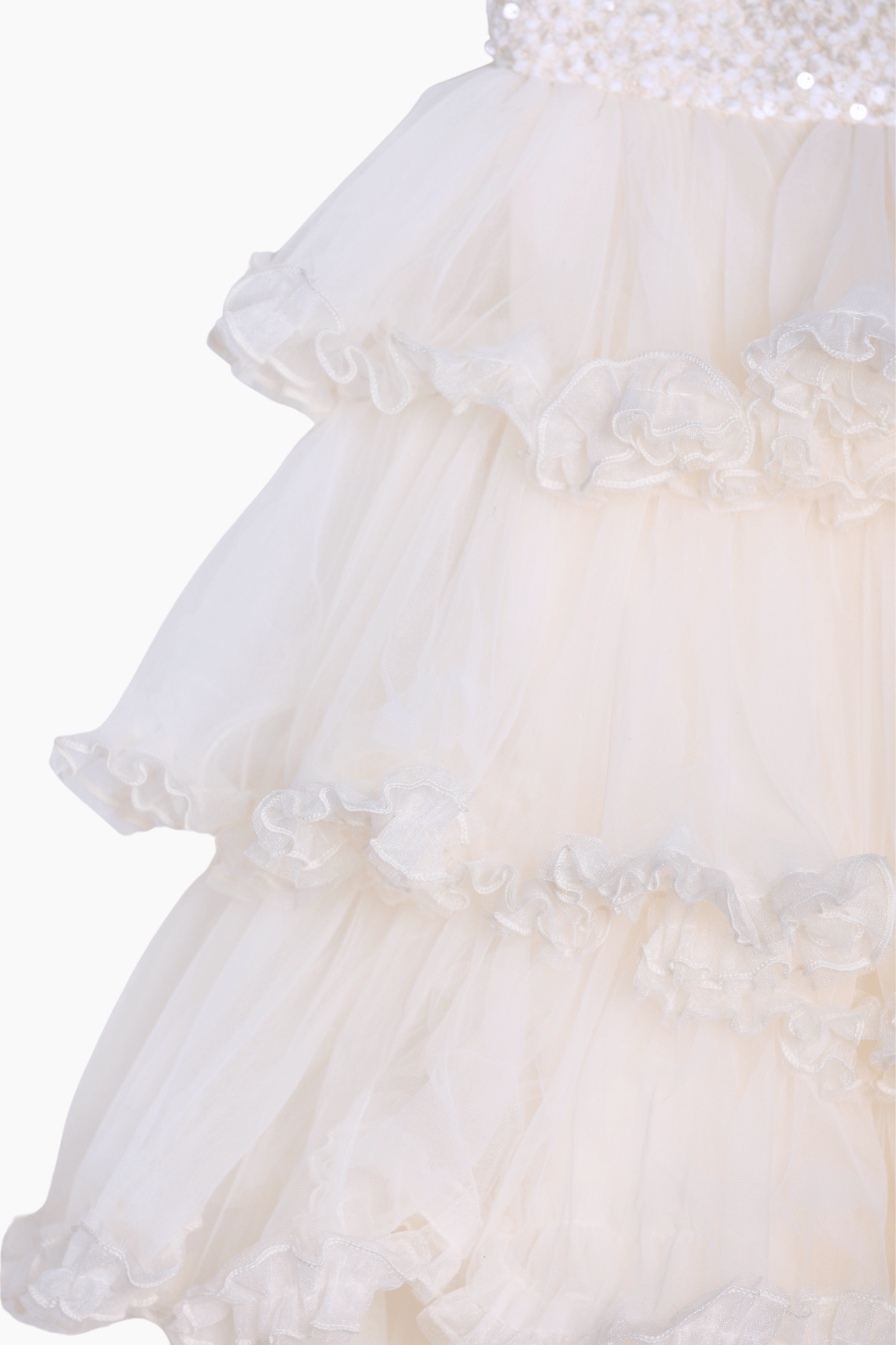 Close-up of the Girls Sparkle Sleeveless Tulle Dress in champagne by KIKI and JOJO, featuring layered tulle, ruffled detailing, and decorative trim, photographed against a plain background.