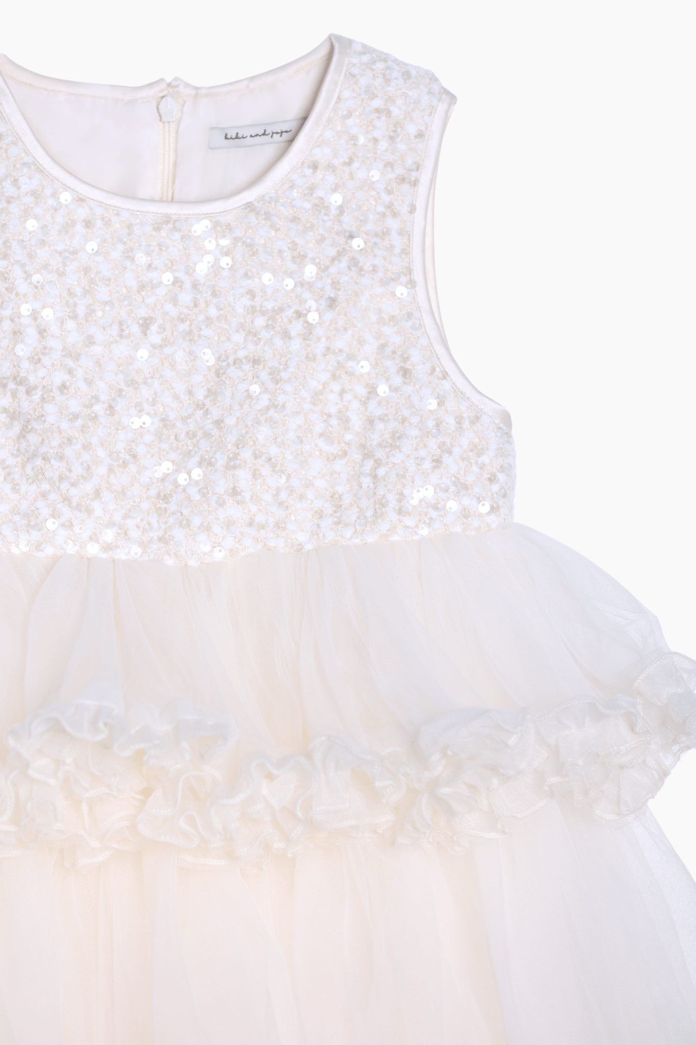 The KIKI and JOJO Girls Sparkle Sleeveless Tulle Dress in Champagne features a sequined bodice, tulle skirt, and ruffled waist detail, displayed against a plain background.