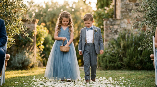 Young flower girl in a dusty blue flower girl dress walking beside a ring bearer in a coordinating dusty blue bow tie and tan suspenders