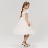 A young girl with braided hair radiates elegance in profile, wearing the KIKI and JOJO Feathered Whisper Dress in blue against a simple light background, paired with light shoes.
