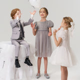 Three children play with a white balloon; one boy sits on a tulle stool while two girls stand nearby, with one wearing the Dusk Whisper Dress by KIKI and JOJO.