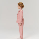 A young boy with light brown hair, wearing KIKI and JOJO Blush Reverie Suit Pants with an adjustable waistband and white sneakers, stands in profile against a plain light background.