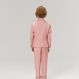 A child with short, light brown hair wears KIKI and JOJO Blush Reverie Suit Pants featuring an adjustable waistband, paired with white sneakers, standing facing away against a plain light background.