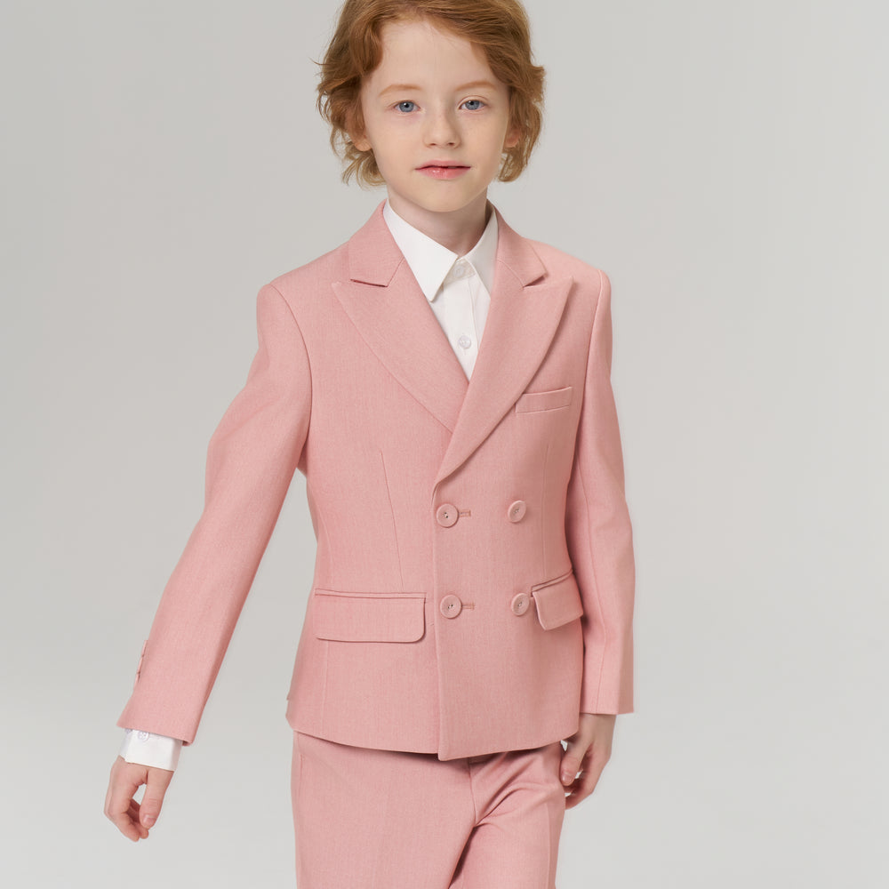 A young child with red hair wearing a light pink suit and white shirt stands against a plain light background.