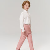 A young child with light brown hair stands against a plain background, wearing a white shirt, KIKI and JOJO Blush Reverie Suit Pants with an adjustable waistband, and white sneakers.