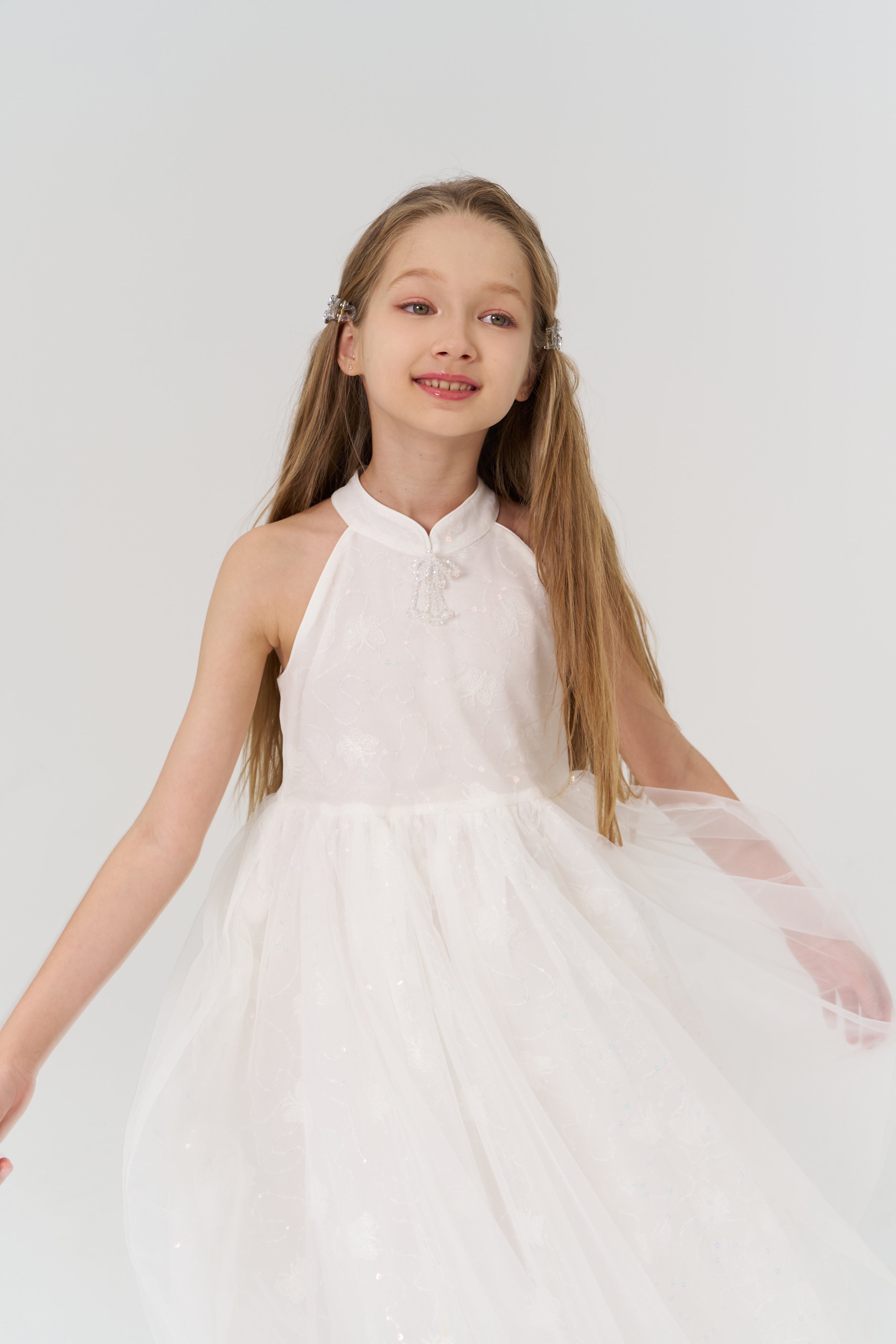 A young girl with long hair gracefully poses in the KIKI and JOJO Butterfly Whispers Dress against a plain white background.