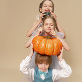 Three children pose in a stack against a beige background; the middle, wearing KIKI and JOJO Celeste Whimsy Suit Pants with an adjustable waistband, balances a pot on their head while the others hold another pot and a pumpkin.