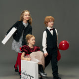 Three children in vintage-inspired luxury: one girl wears the KIKI and JOJO Girls Tweed Jacket – Classic Black Pearl, sitting in a wheeled box; another girl pushes it, while a boy stands beside them holding a red balloon.
