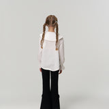 A young girl with braided hair faces away, wearing KIKI and JOJO's Petal Whisper Dress Pants—flared black with an elastic waistband—and a white blouse, set against a plain light background.