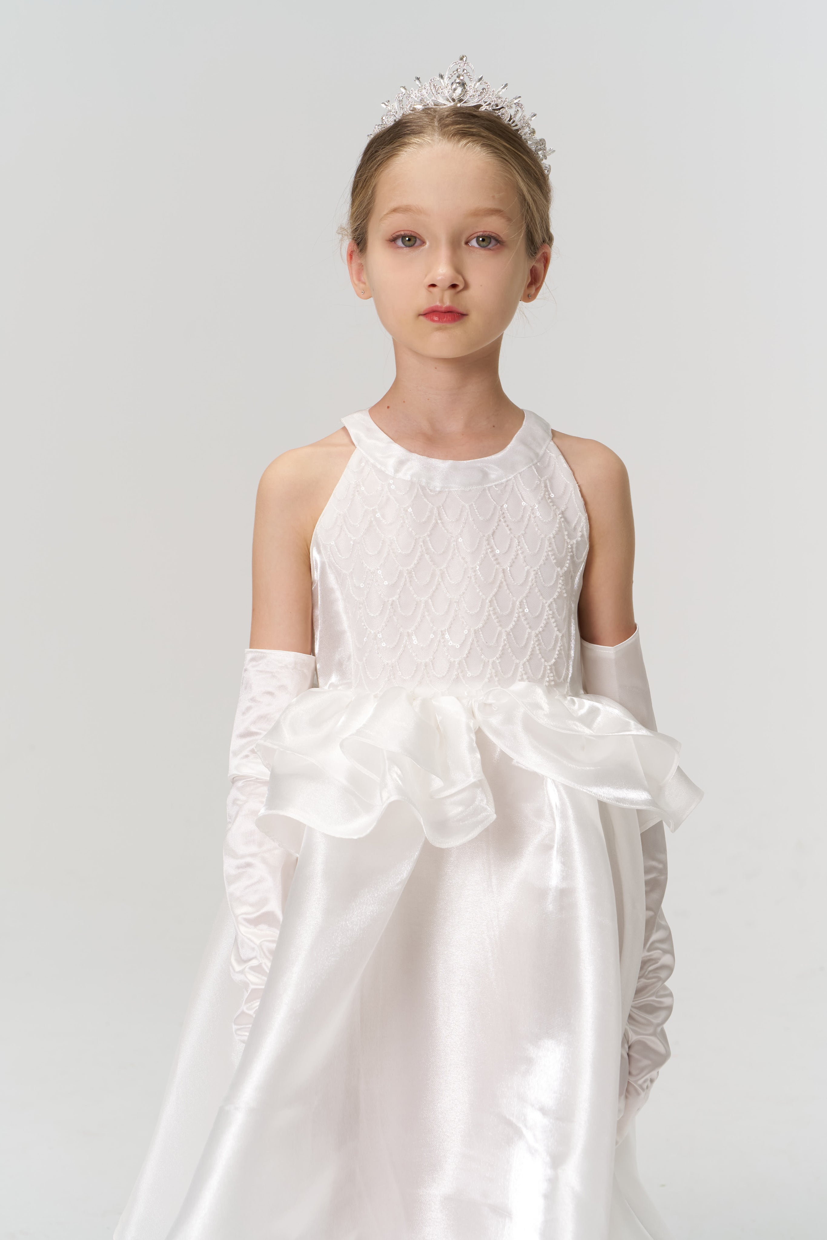 A young girl in the Pearl Glow Whisper Dress by KIKI and JOJO, featuring delicate beaded embroidery, stands against a plain white background, looking directly at the camera.