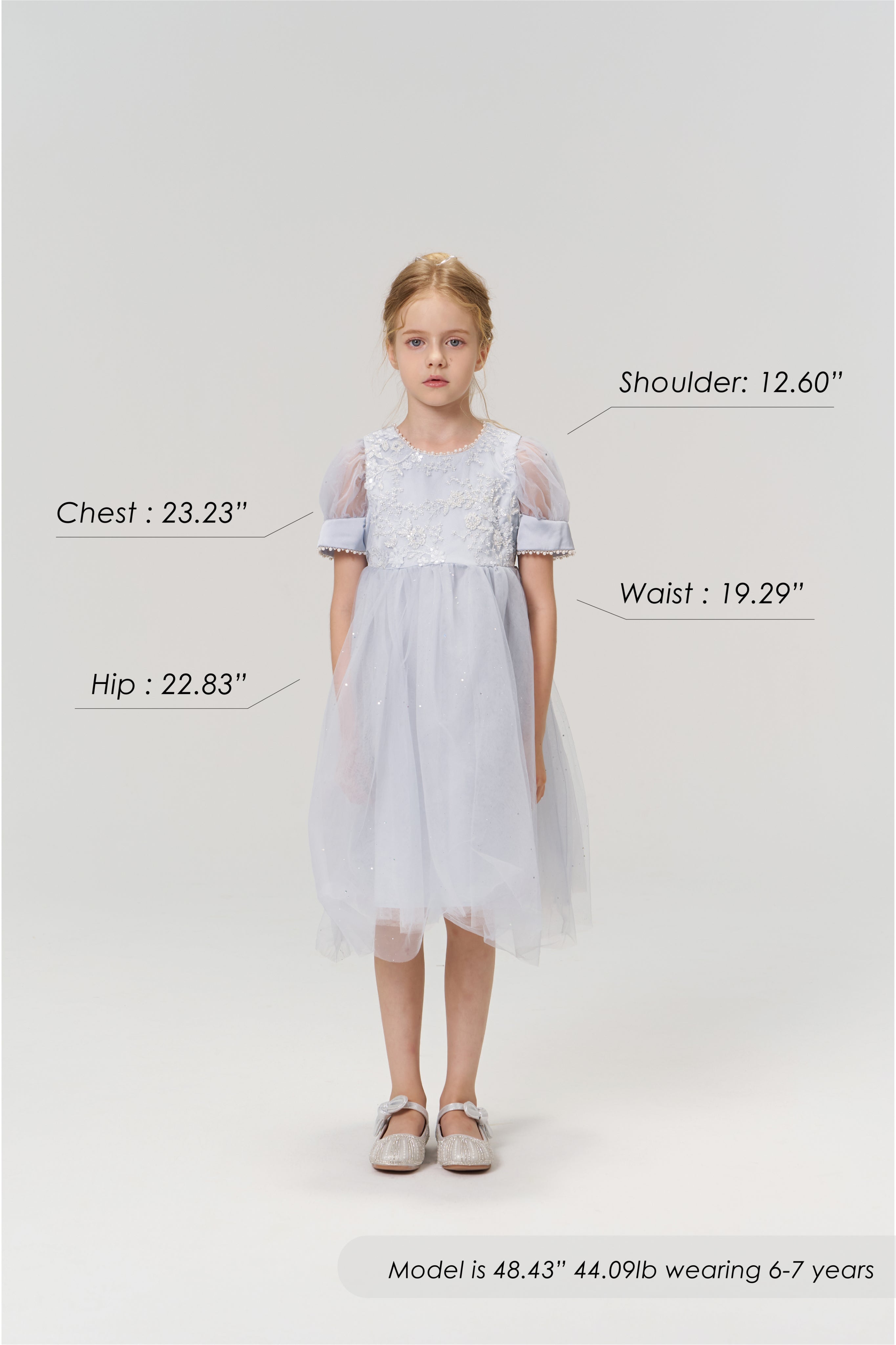 A young girl aged 6-7 models the Mist Whisper Dress by KIKI and JOJO in light blue with silver shoes, standing against a plain background. Her chest, hip, shoulder, and waist measurements are labeled for size reference.