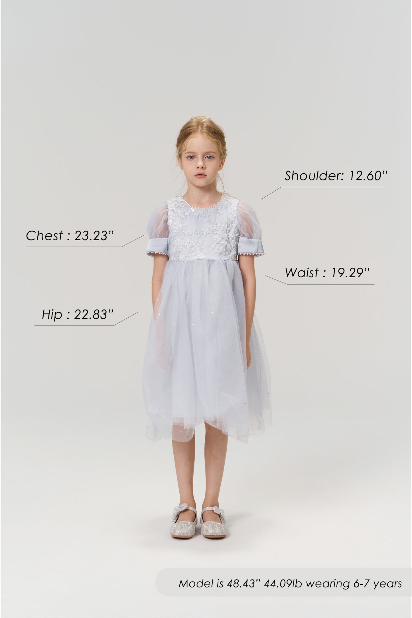 A young girl aged 6-7 models the Mist Whisper Dress by KIKI and JOJO in light blue with silver shoes, standing against a plain background. Her chest, hip, shoulder, and waist measurements are labeled for size reference.
