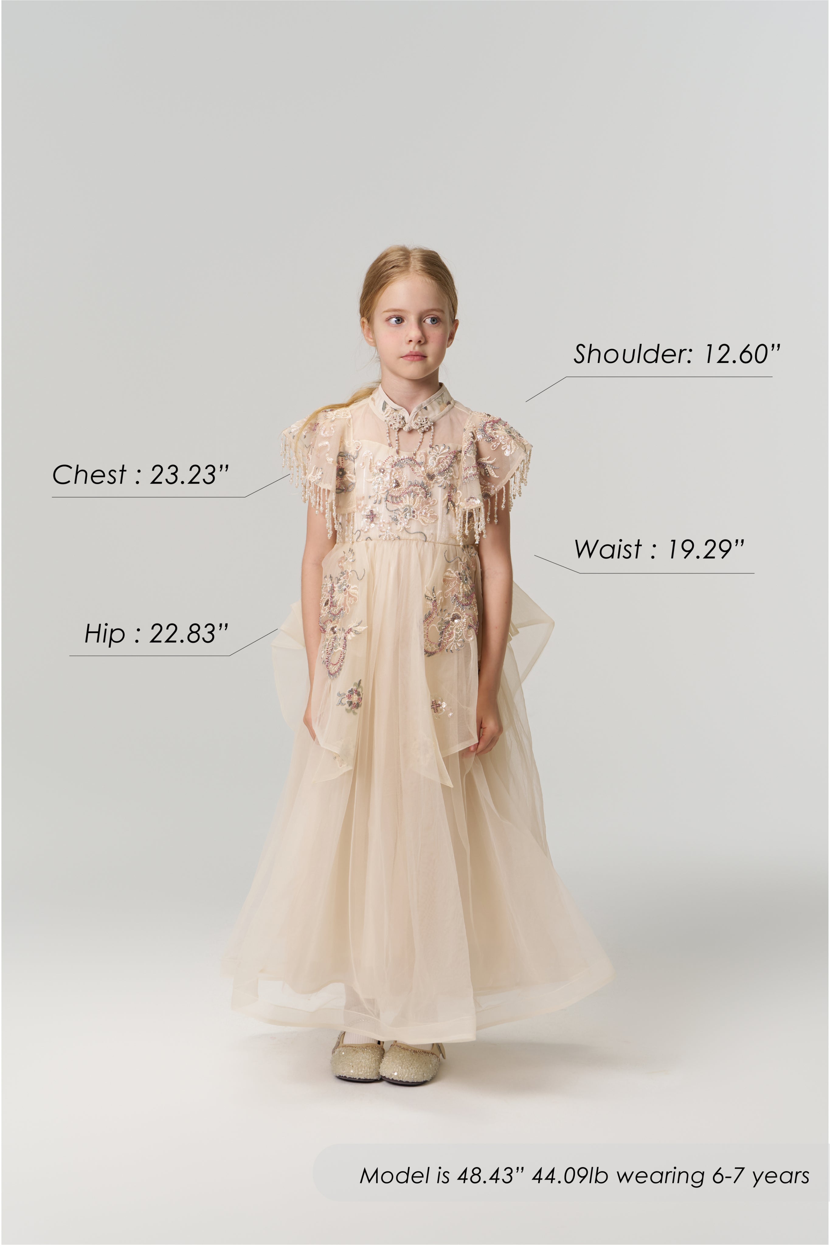 A young girl faces forward wearing the Jade Whisper Dress by KIKI and JOJO, a cream-colored cheongsam with floral embroidery and a mandarin collar. Her body measurements and model details are labeled around her in the image.