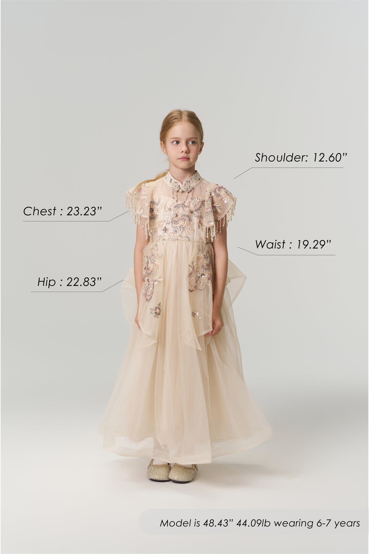 A young girl faces forward wearing the Jade Whisper Dress by KIKI and JOJO, a cream-colored cheongsam with floral embroidery and a mandarin collar. Her body measurements and model details are labeled around her in the image.