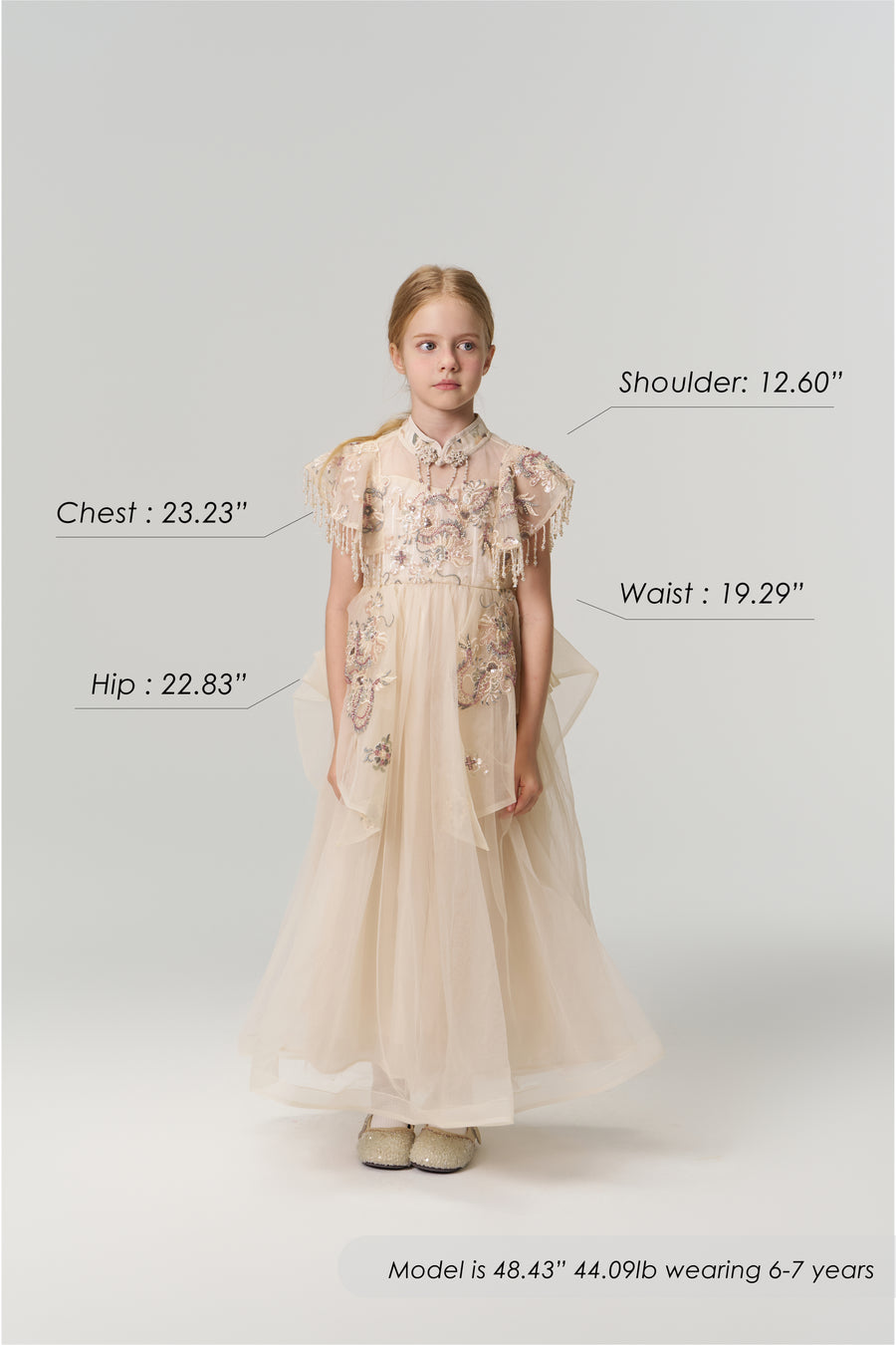 A young girl faces forward wearing the Jade Whisper Dress by KIKI and JOJO, a cream-colored cheongsam with floral embroidery and a mandarin collar. Her body measurements and model details are labeled around her in the image.