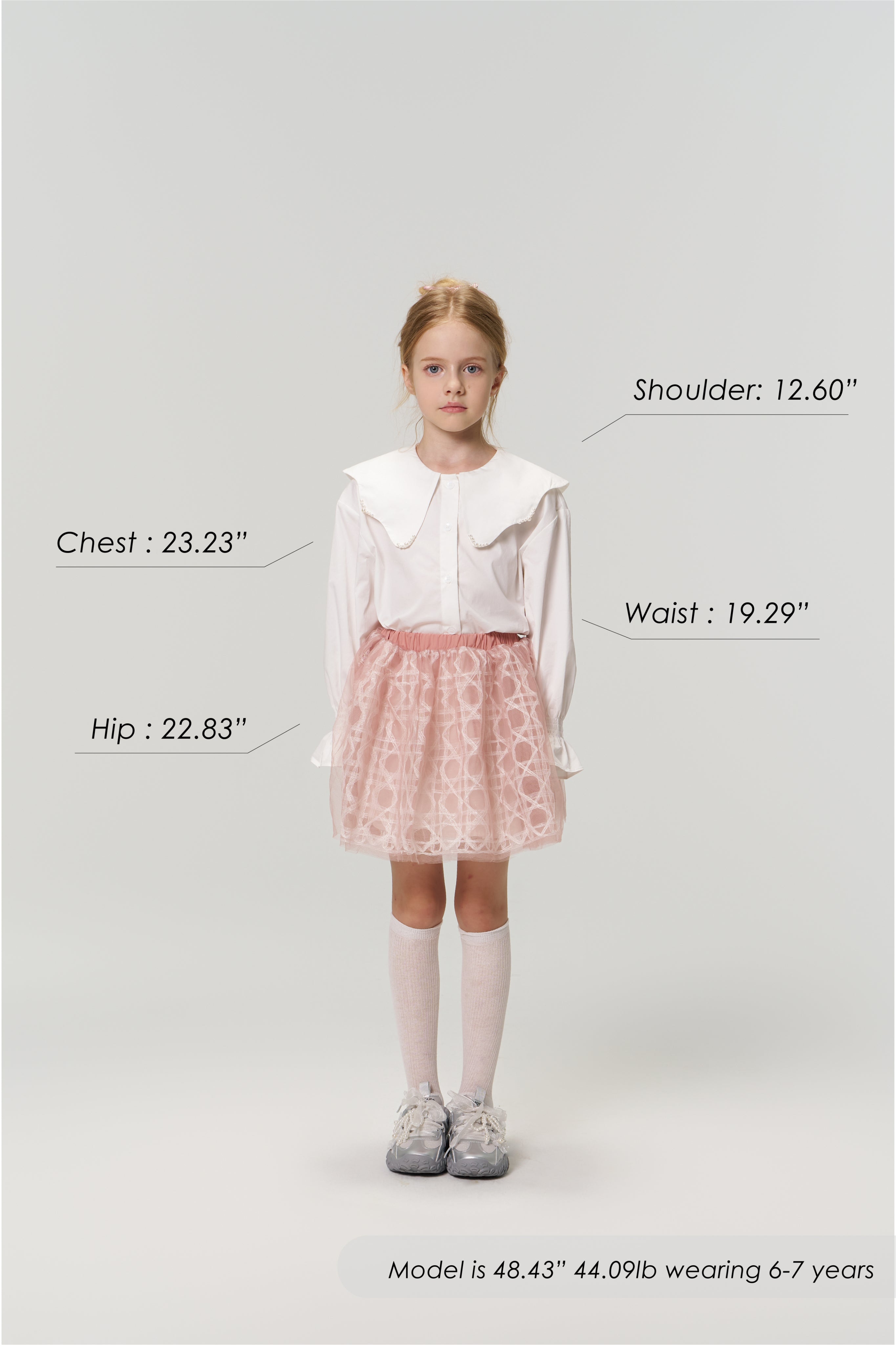 A young girl faces forward wearing the KIKI and JOJO Moonlit Whisper Blouse with puffed lantern sleeves and a pink skirt. Her body measurements plus height, weight, and age are labeled around her.