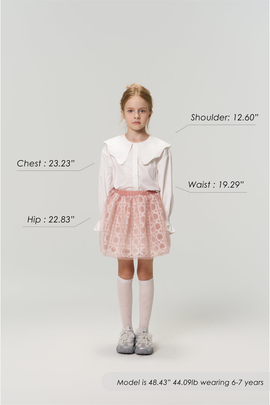 A young girl faces forward wearing the KIKI and JOJO Moonlit Whisper Blouse with puffed lantern sleeves and a pink skirt. Her body measurements plus height, weight, and age are labeled around her.