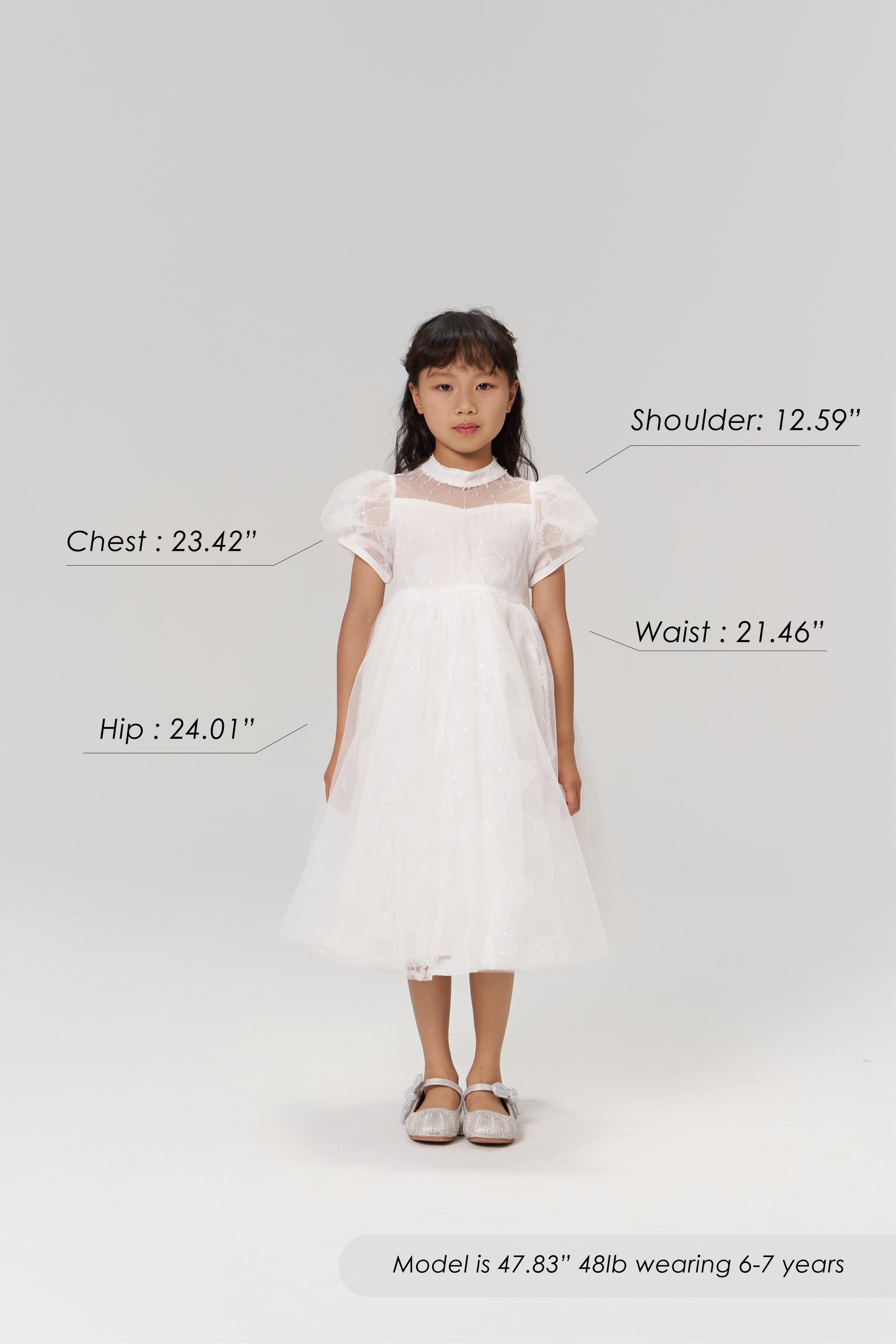 A young girl faces forward in the KIKI and JOJO Whisper Bloom Dress, chest 23.42", shoulder 12.59", waist 21.46", hip 24.01". Model is 47.83" tall, weighs 48lb, and wears size 6-7 years.