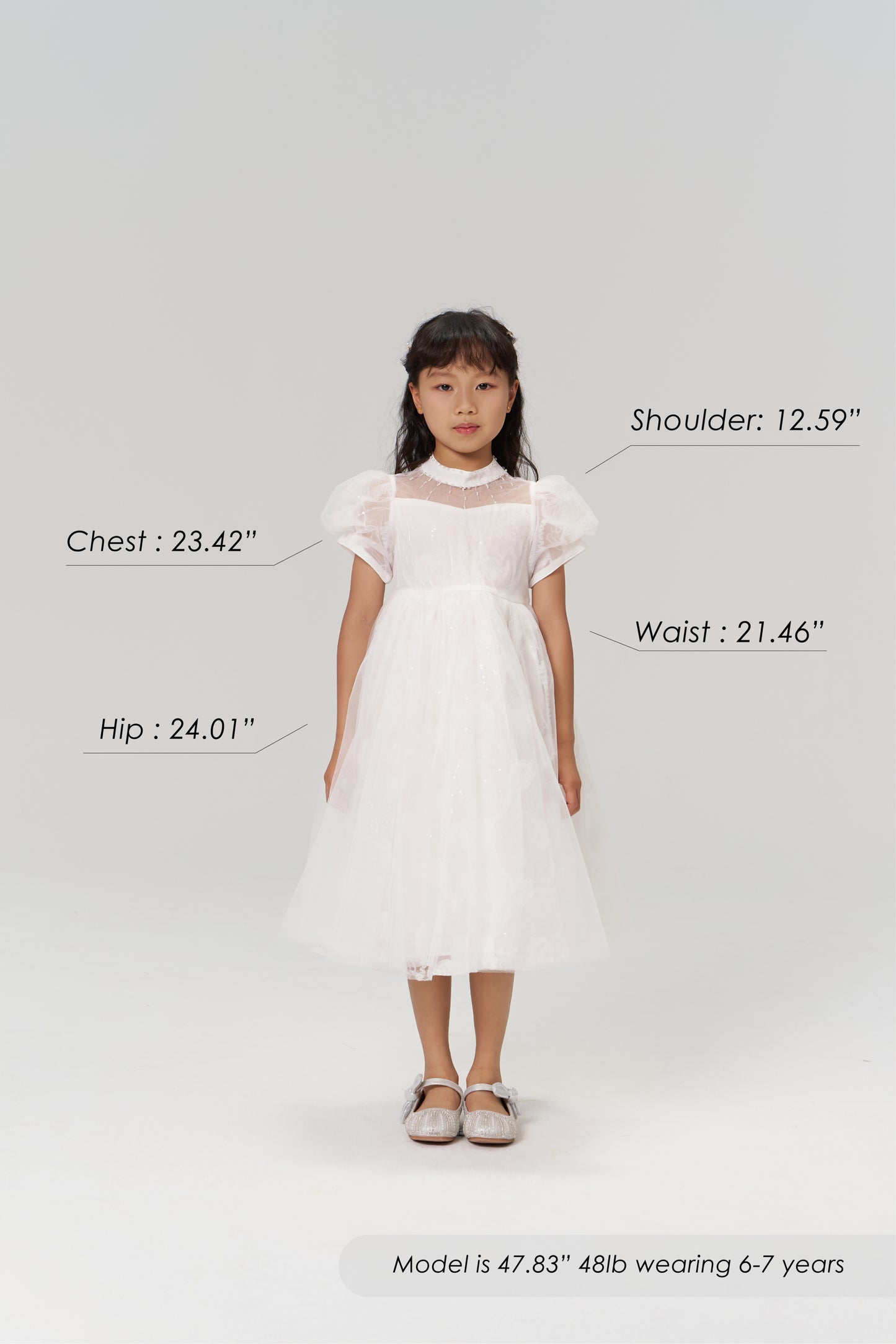 A young girl faces forward in the KIKI and JOJO Whisper Bloom Dress, chest 23.42", shoulder 12.59", waist 21.46", hip 24.01". Model is 47.83" tall, weighs 48lb, and wears size 6-7 years.
