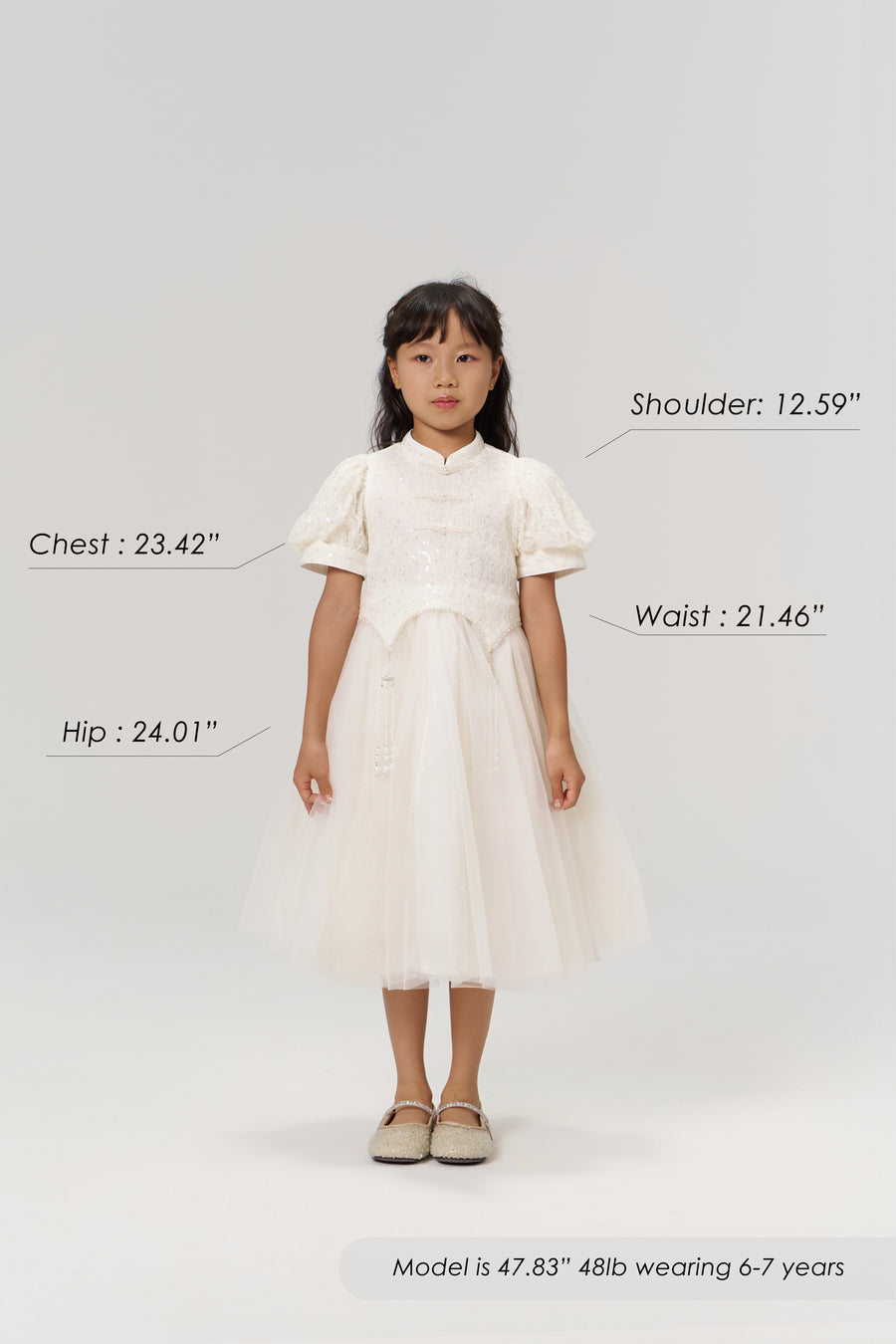 A young girl faces forward in the Orchid Whisper Dress by KIKI and JOJO with beige shoes; her height, weight, age, and body measurements are labeled around her on a plain light background.
