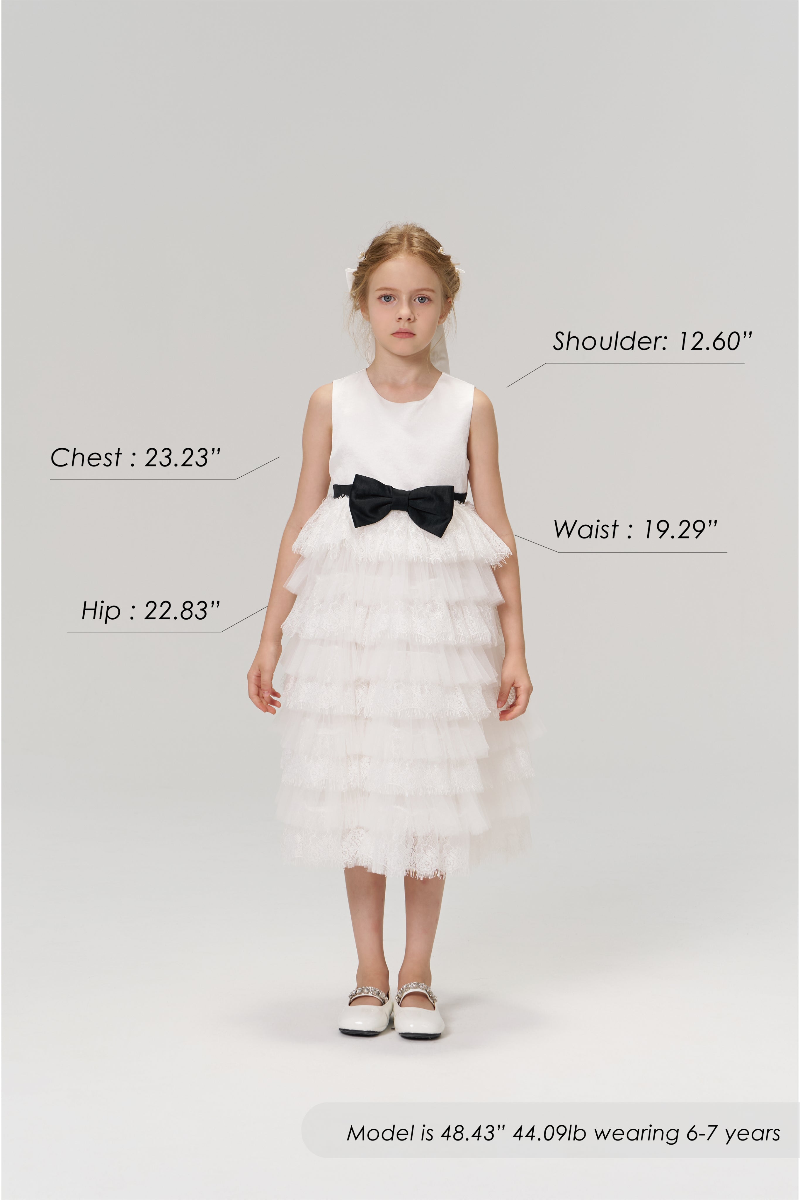 A young girl models the KIKI and JOJO Monochrome Whisper Dress, a black and white layered style with a tulle cake skirt. Shown with size chart for shoulder, chest, waist, and hip. Model is 48.43", 44.09 lb, wearing size 6–7 years.