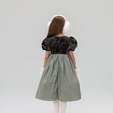 A young girl wears the KIKI and JOJO Girls Velvet Puff Sleeve Dress with Rhinestone Trim in Forest Green, styled with white tights, silver shoes, and white earmuffs and cuffs, standing against a plain background.