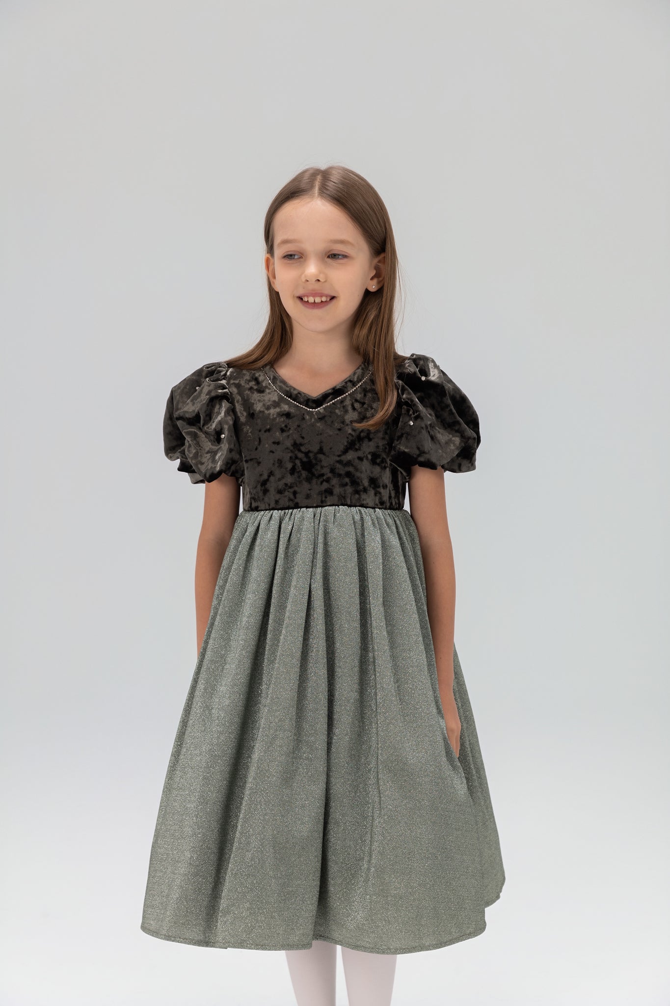 A young girl stands against a plain light background wearing the KIKI and JOJO Girls Velvet Puff Sleeve Dress with Rhinestone Trim in forest green.