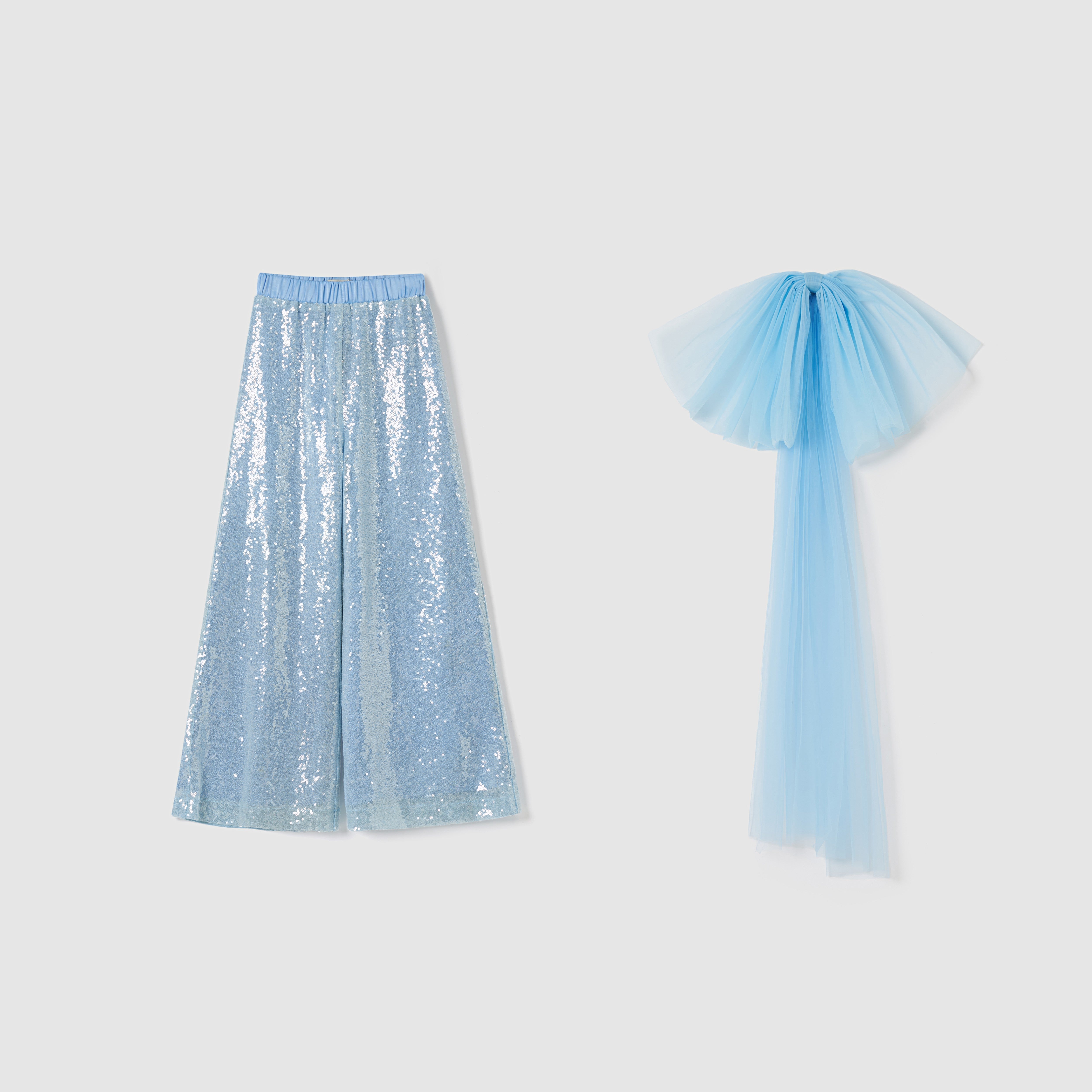 The KIKI and JOJO Radiance Sequin Wide-leg Pants feature a light blue high-rise, wide-leg silhouette with a matching detachable bow train and blue tulle sash, shown on a plain white background.