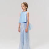 A young girl poses in a studio wearing KIKI and JOJO’s Radiance Sequin Wide-leg Pants, a sleeveless light blue top, and white shoes, all set against a simple light-colored backdrop.
