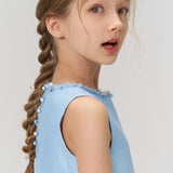 A young girl with braided hair and floral hairpins wears the KIKI and JOJO Radiance Satin Crop Top in light blue, looking slightly over her shoulder—a stunning pick for holiday parties.