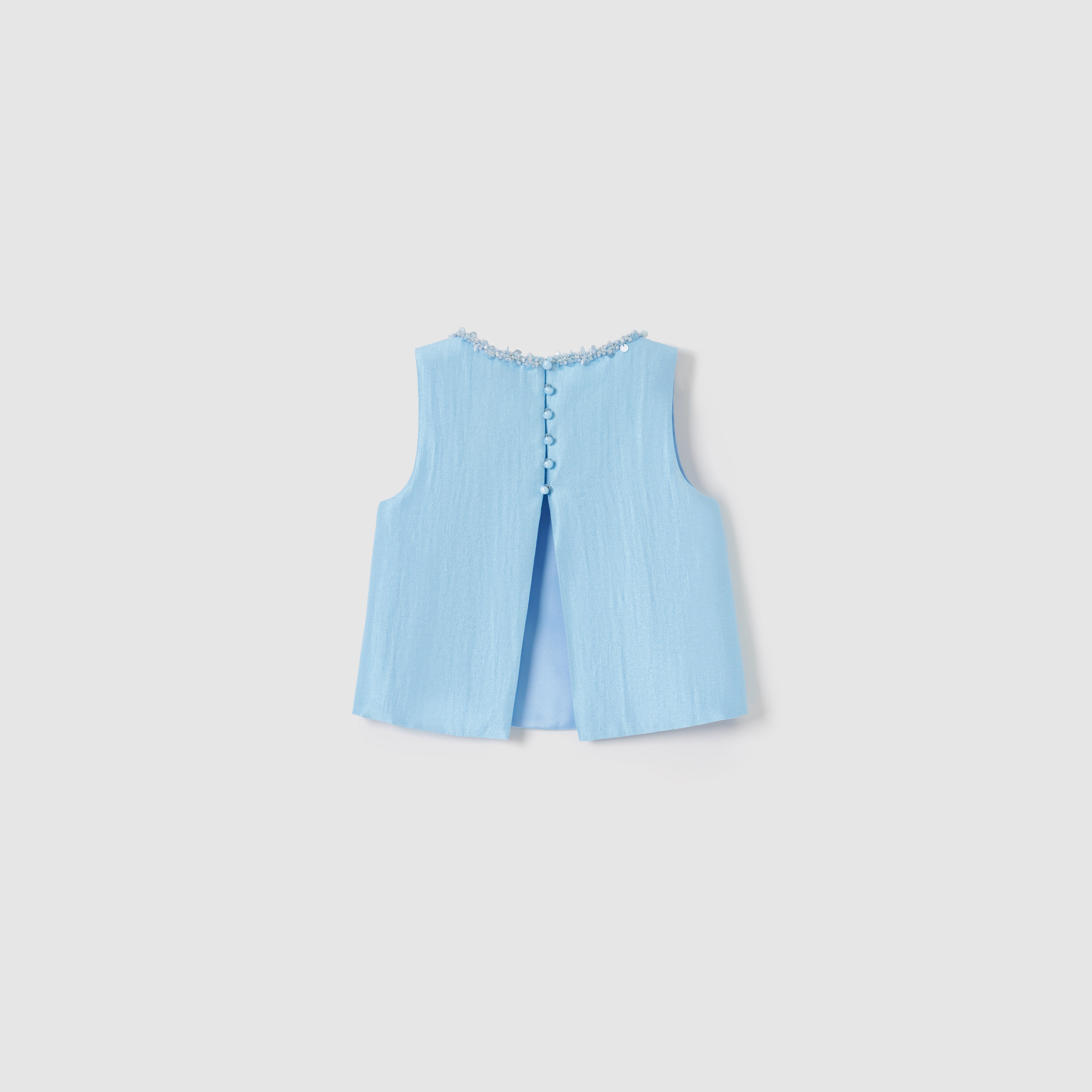 The Radiance Satin Crop Top by KIKI and JOJO is a sleeveless light blue luminous top with textured fabric, decorative buttons, floral neckline trim, and a subtle back slit.