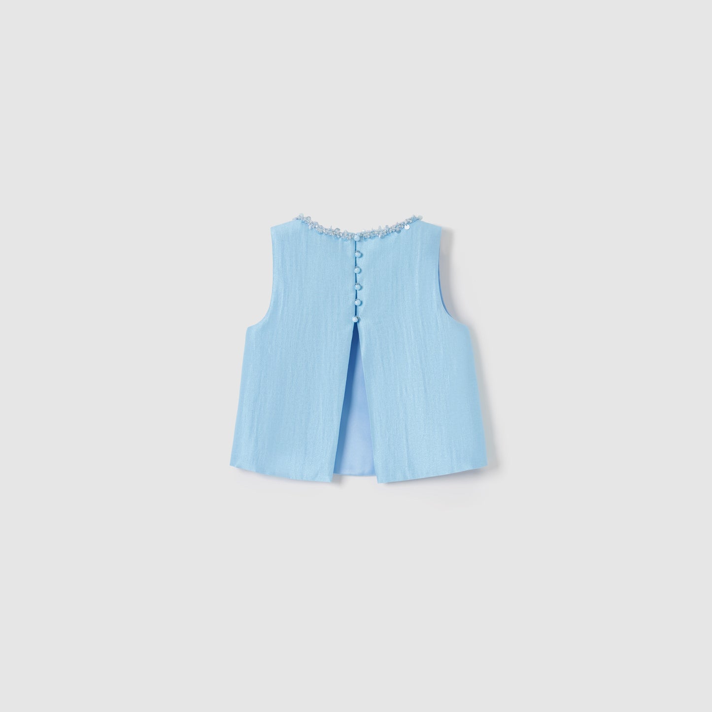 The Radiance Satin Crop Top by KIKI and JOJO is a sleeveless light blue luminous top with textured fabric, decorative buttons, floral neckline trim, and a subtle back slit.