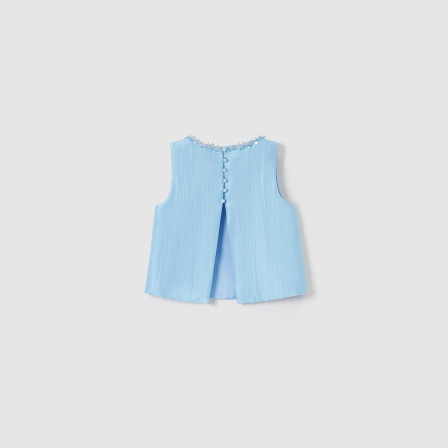 The Radiance Satin Crop Top by KIKI and JOJO is a sleeveless light blue luminous top with textured fabric, decorative buttons, floral neckline trim, and a subtle back slit.