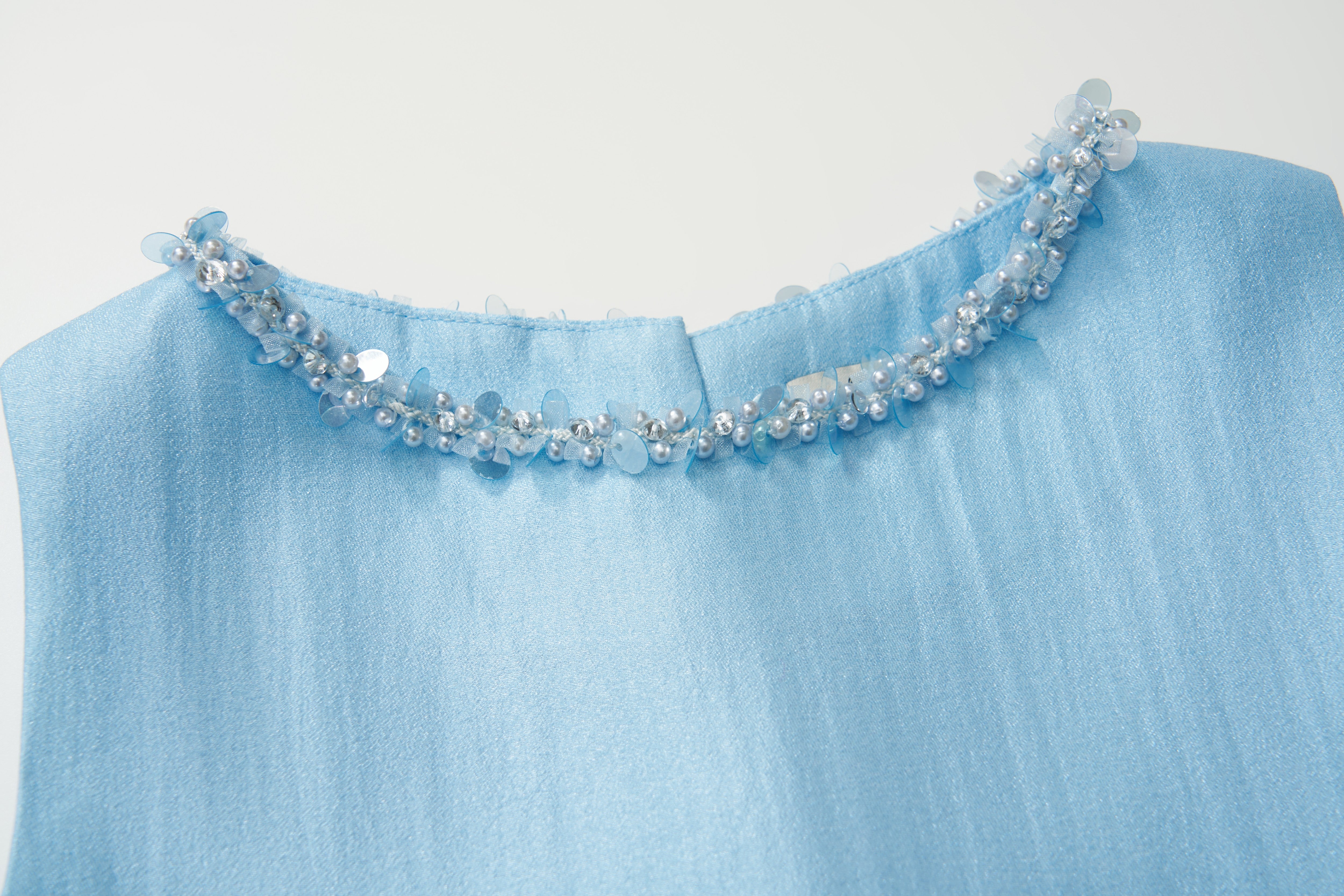 A close-up of the Radiance Satin Crop Top by KIKI and JOJO in light blue, highlighting its hand-beaded pearl neckline with small blue beads and sequins.