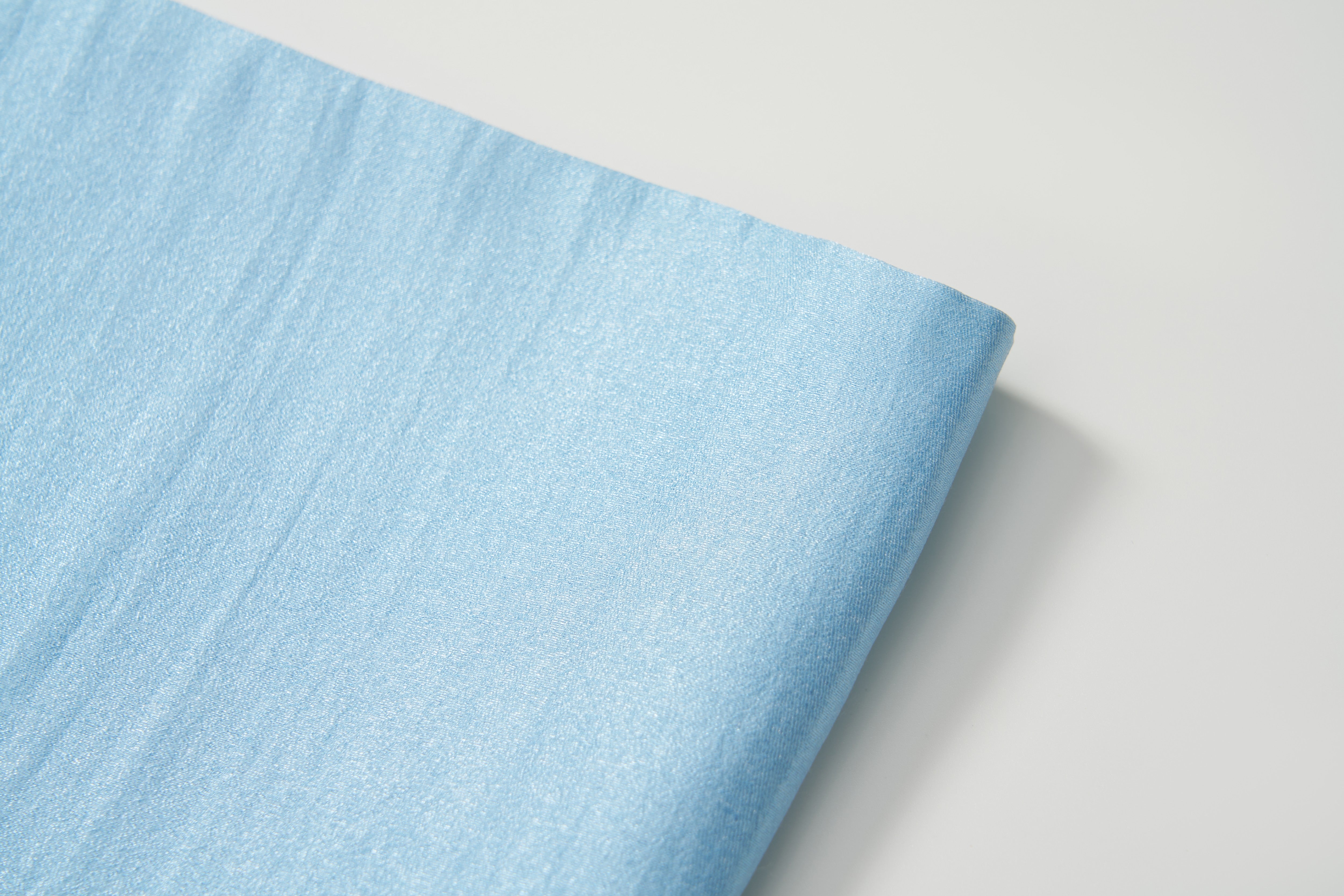 The Radiance Satin Crop Top by KIKI and JOJO, made from light blue liquid-sheen satin, is shown folded on a white surface.